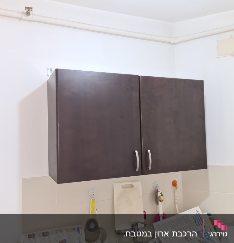 ארון מטבח כהה עם ידיות מתכת, כיור וברז